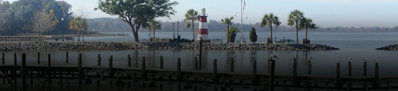 Wooden pier extending into a lake with a small striped lighthouse in the background.