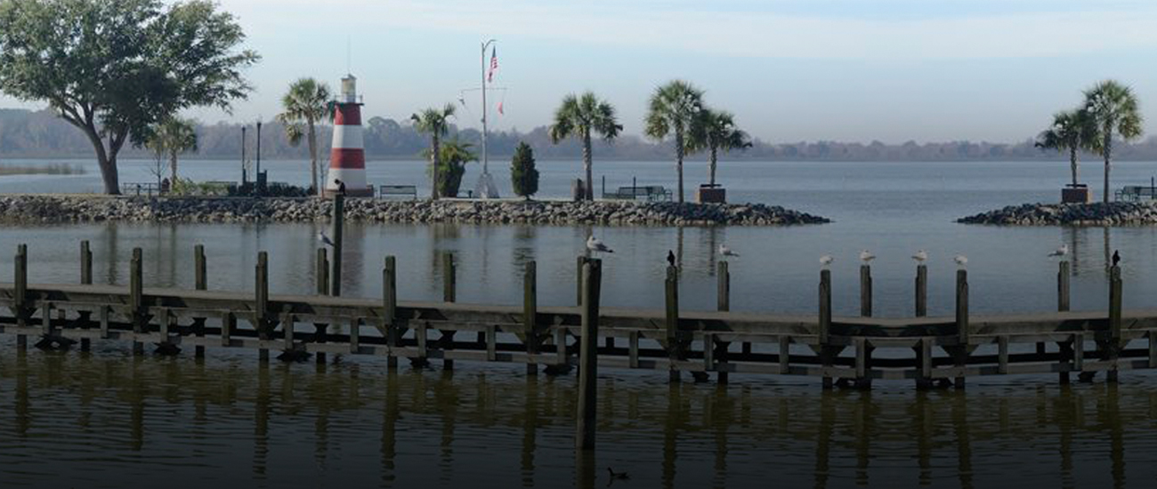 Wooden pier extending into a lake with a small striped lighthouse in the background.